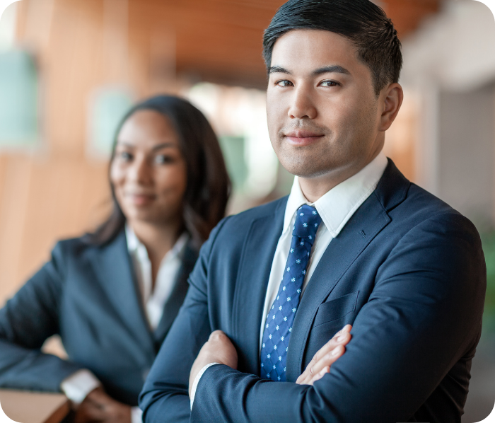 Businessman smiling at the camera with arms crossed. His female colleague looks onward.