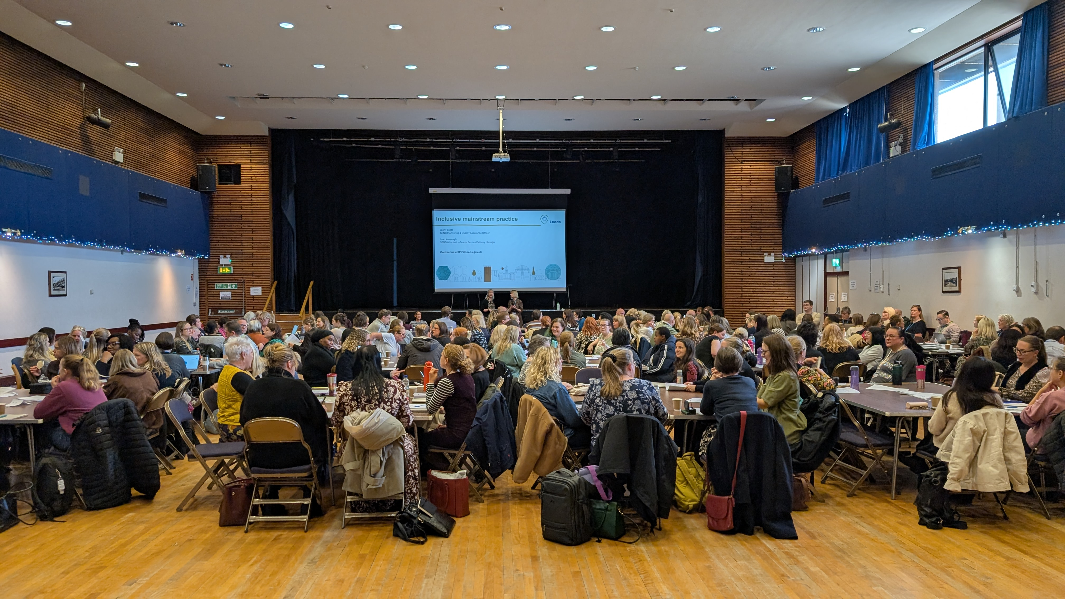 people sitting banquet style in a ballroom with a large screen