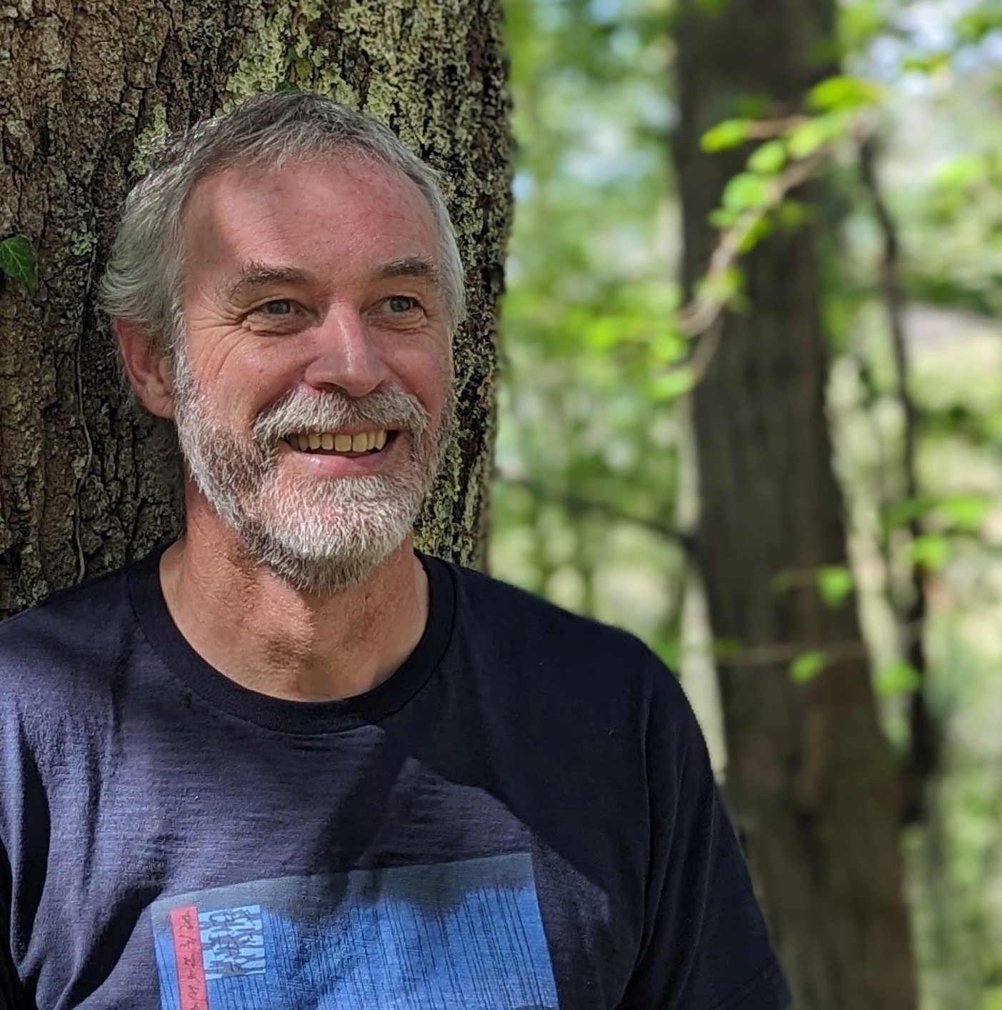 Jonny is standing in the partial shade of a tree