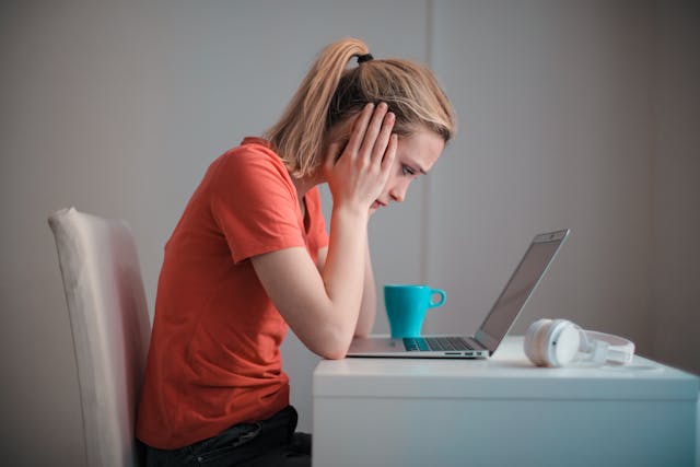 a woman with her head in her hands stares at her laptop