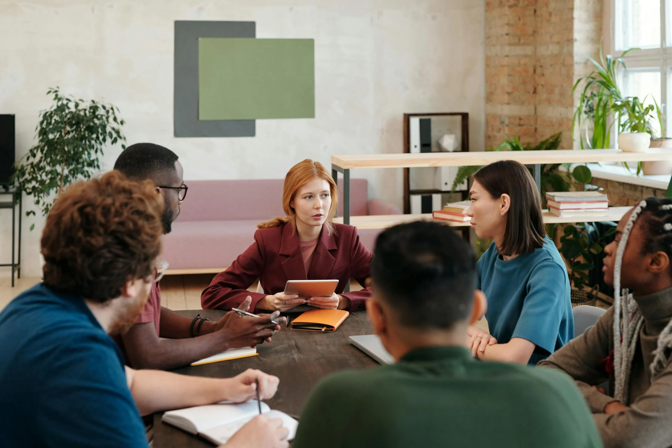 Kolleg:innen die in einem Meeting um einen Tisch herum sitzen