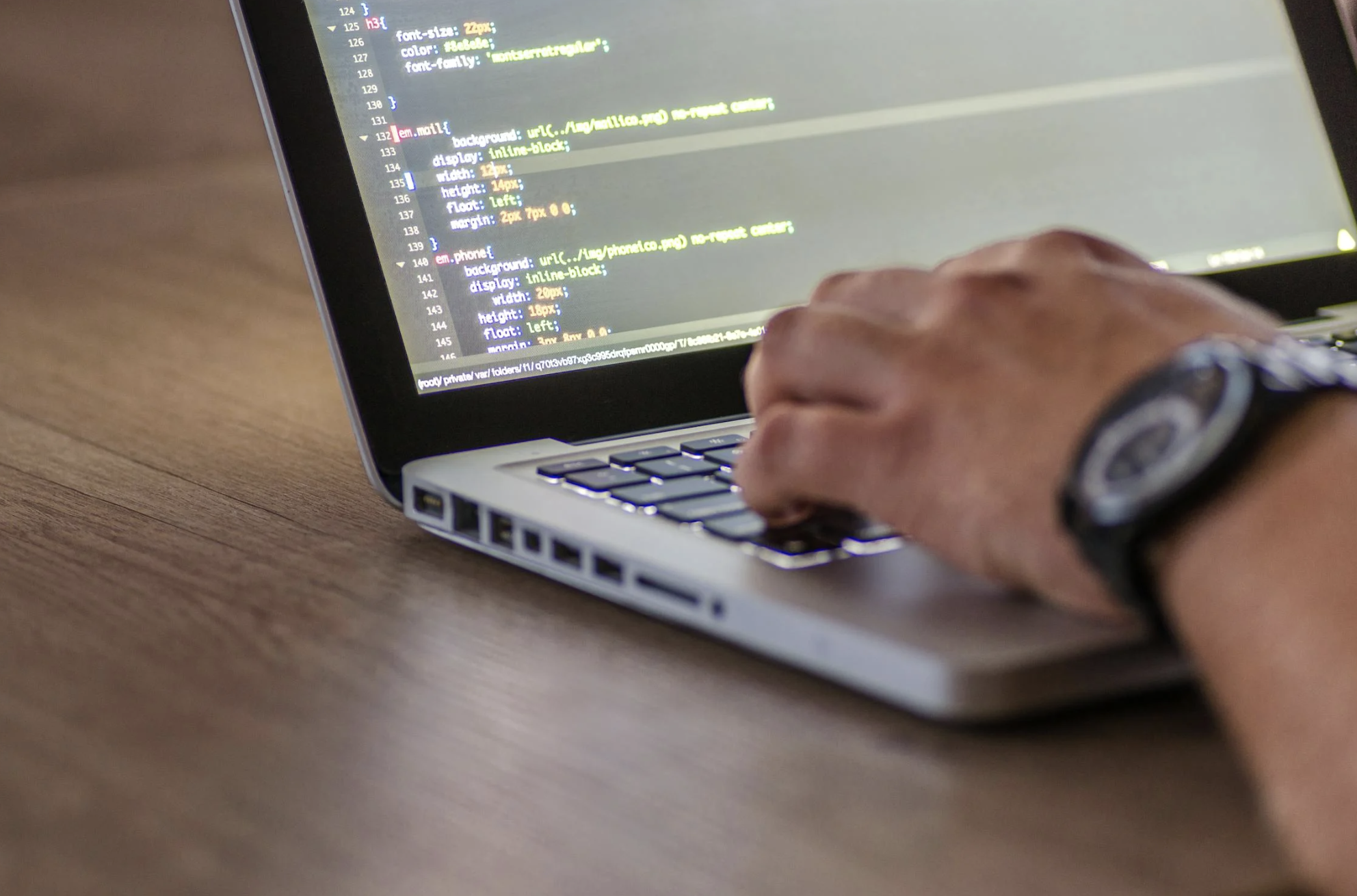 Ein Mensch programmiert an einem Laptop. Zu sehen ist nur die Hand des Menschen die auf der Tastatur des Laptops liegt und ein kleiner Teil des Bildschirms des Laptops.