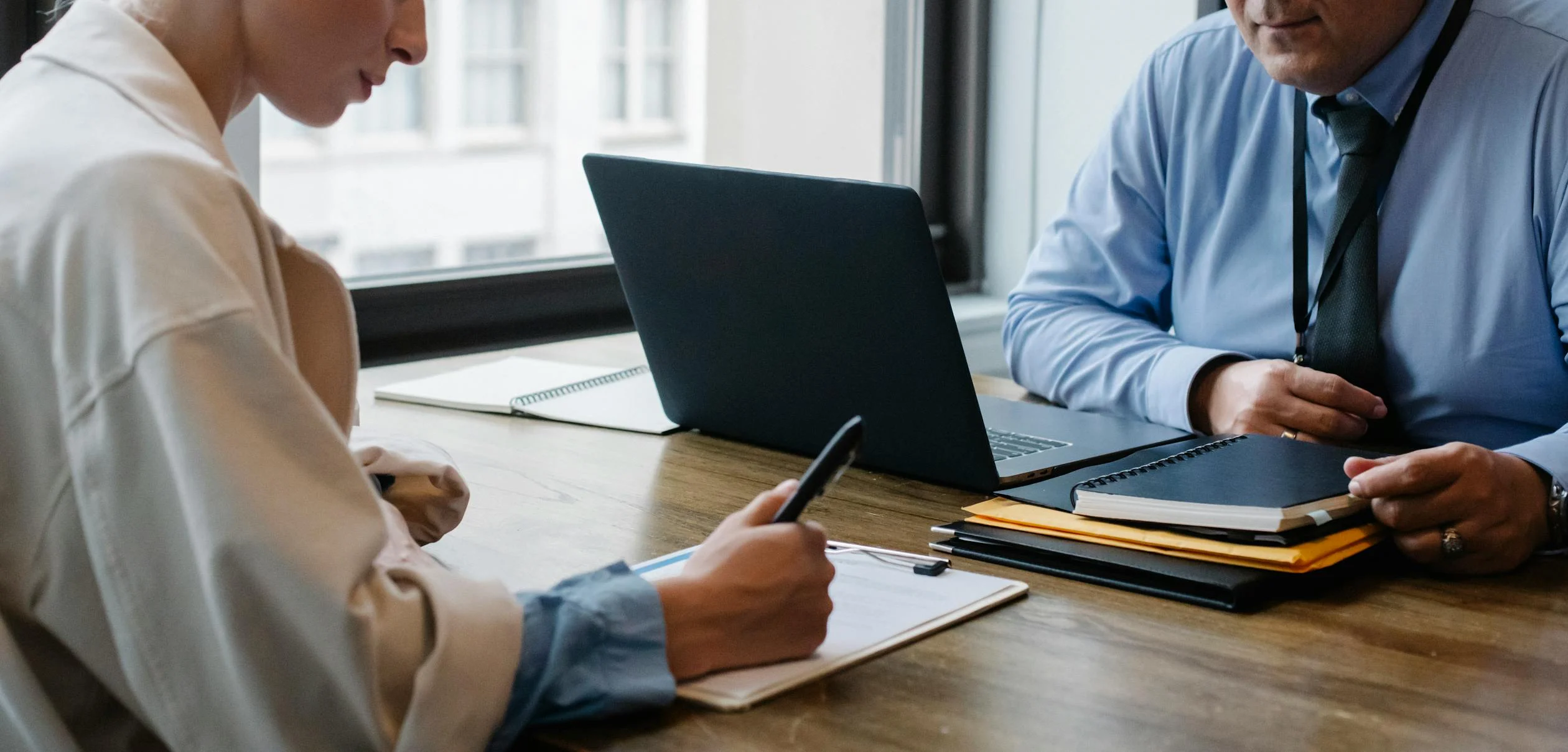 Zwei Kolleg:innen sitzen sich an einem Tisch gegenüber uind arbeiten