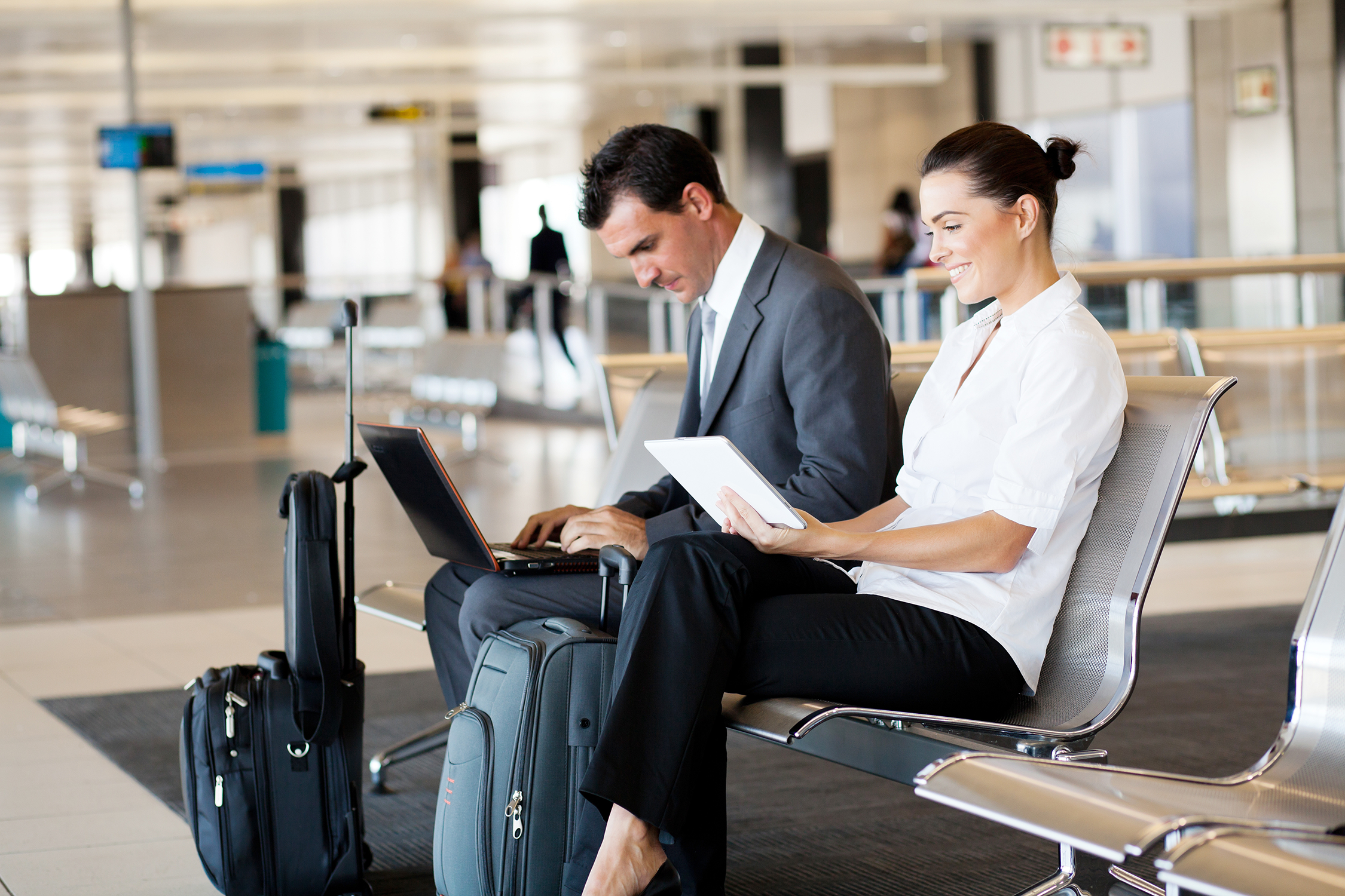 Menschen die auf einer Bank am Flughafen sitzen und an Laptop und Tablet arbeiten