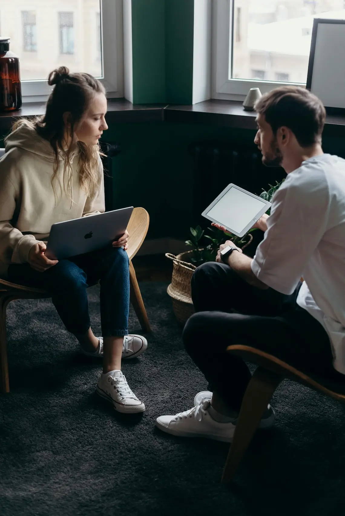 Zwei Kolleg:innen mit Laptop und Tablet in der Hand, die sich gegenüber sitzen