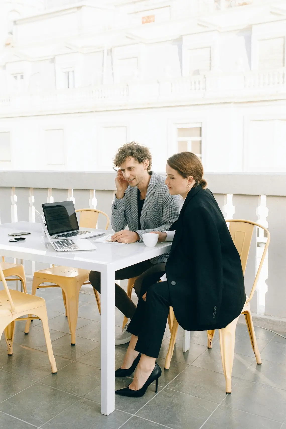 Zwei Kolleg:innen sitzen an einem Tisch und schauen gemeinsam auf einen Laptop