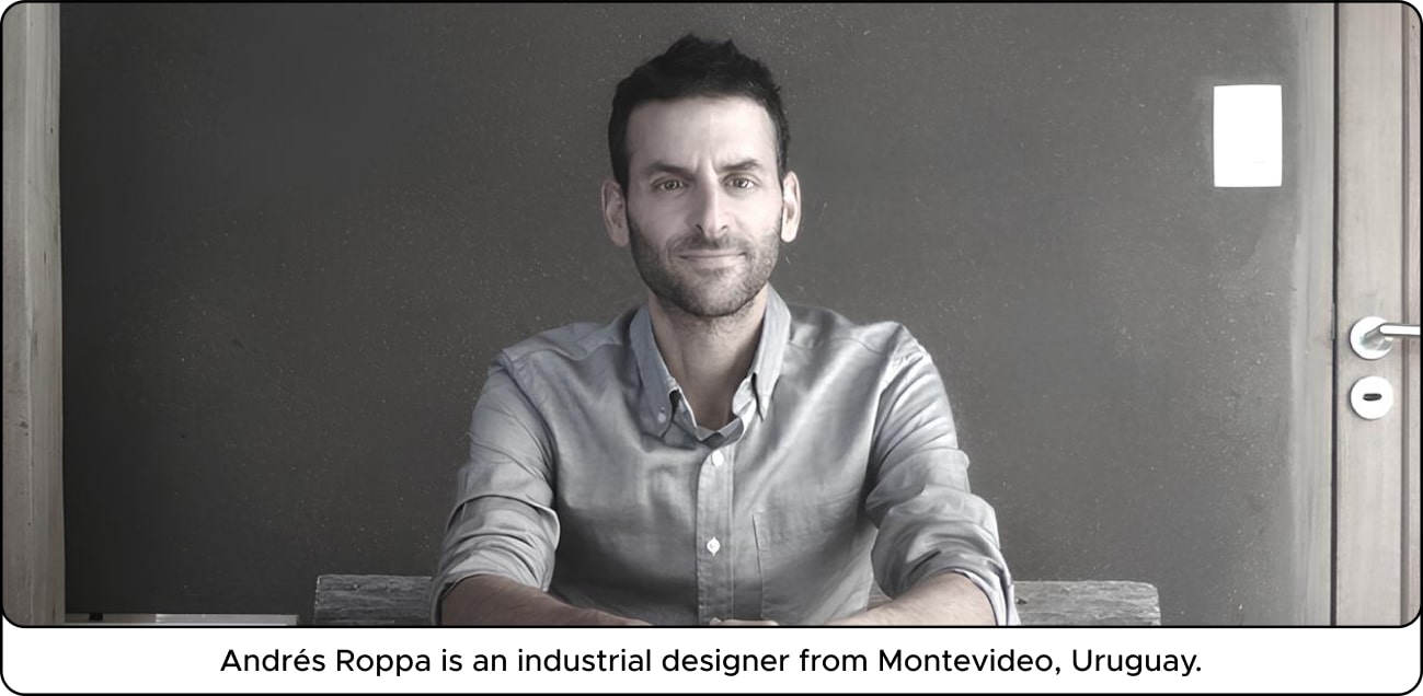 A man sitting at a table against a dark wall, wearing a light shirt, with a neutral expression.